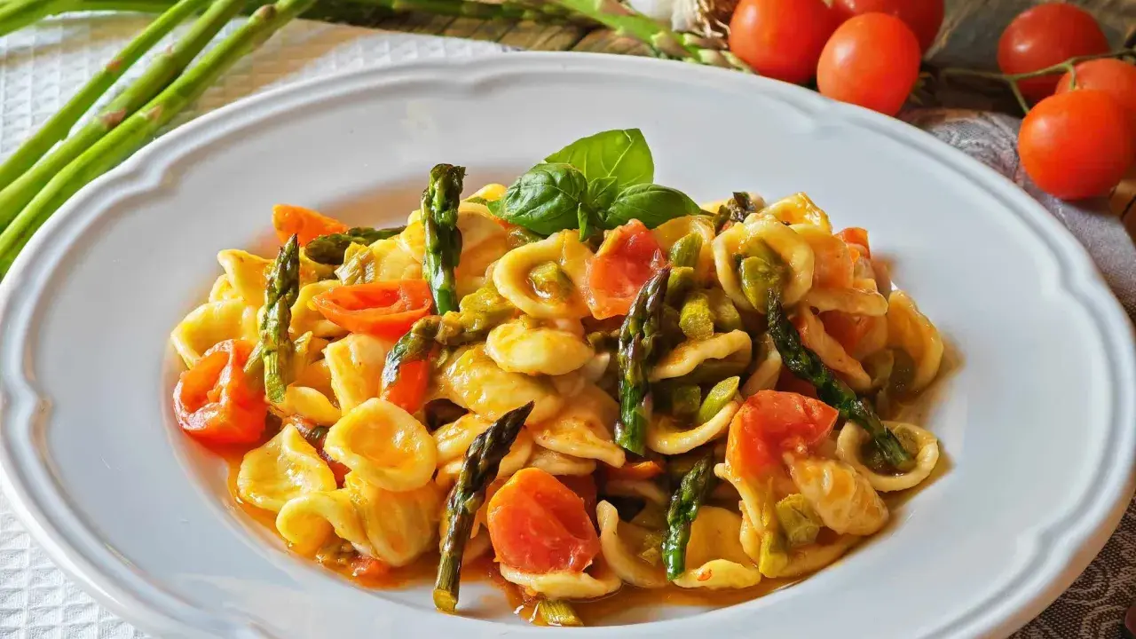 Piatto di orecchiette con asparagi freschi e pomodorini succosi, guarnito con basilico. Un classico della cucina italiana.