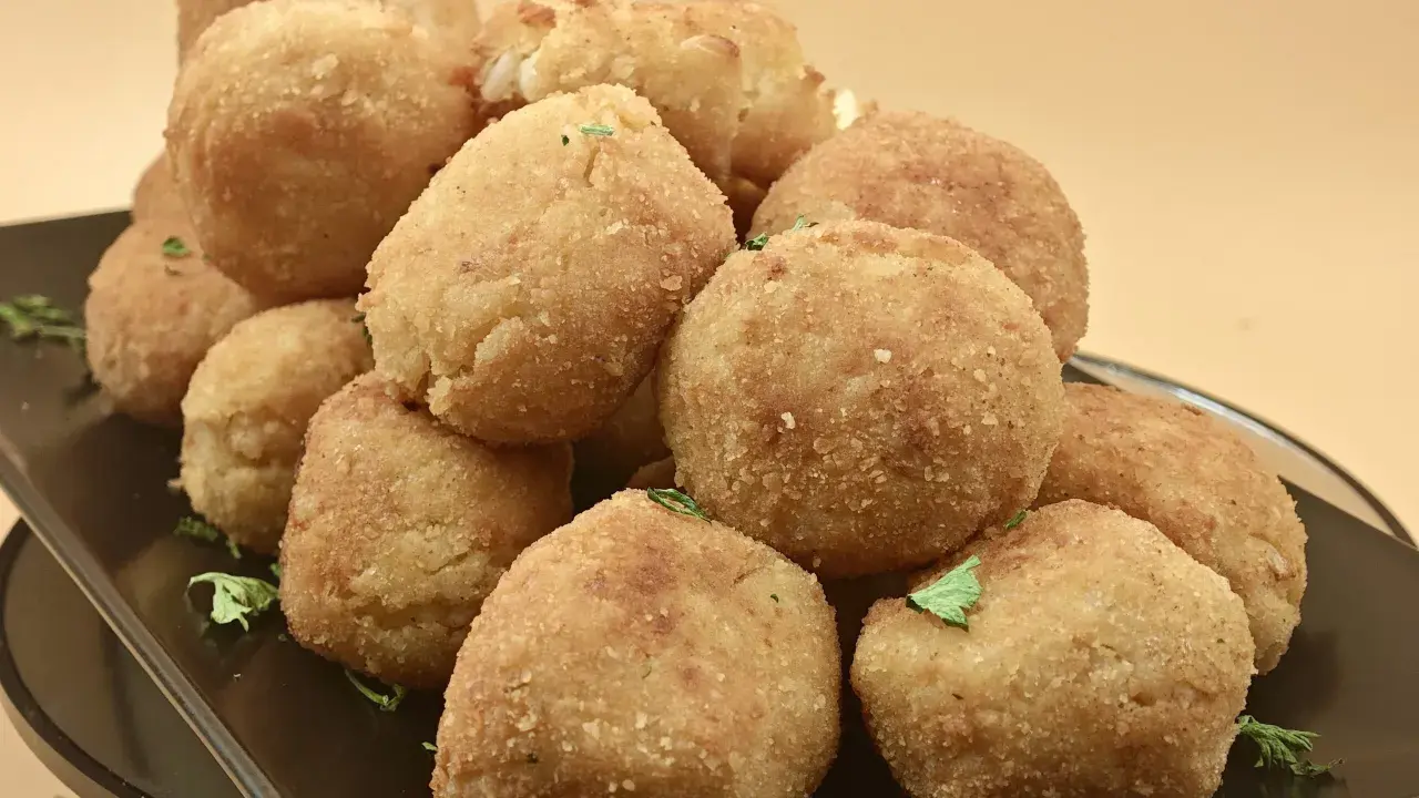 Un mucchio invitante di polpette di riso dorate e croccanti, guarnite con prezzemolo fresco, su un piatto scuro.