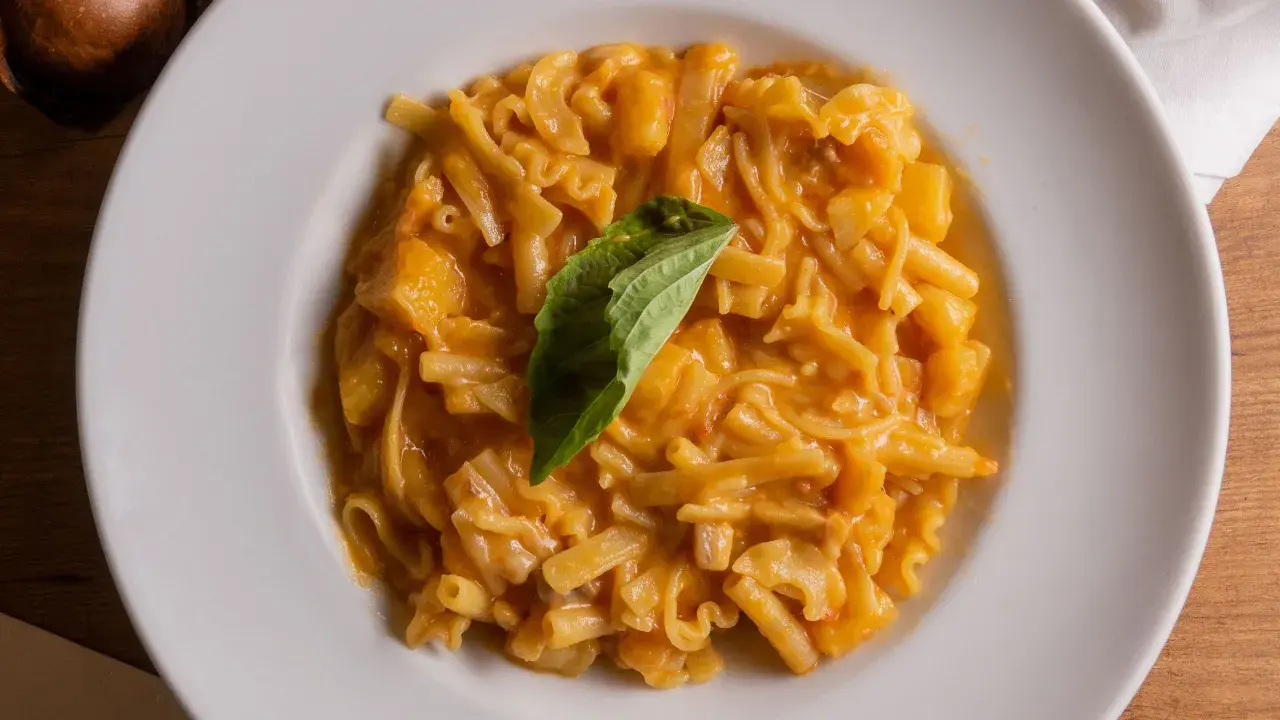 Un piatto di pasta patate e provola cremoso, con pezzi di patate e un rametto di basilico fresco.
