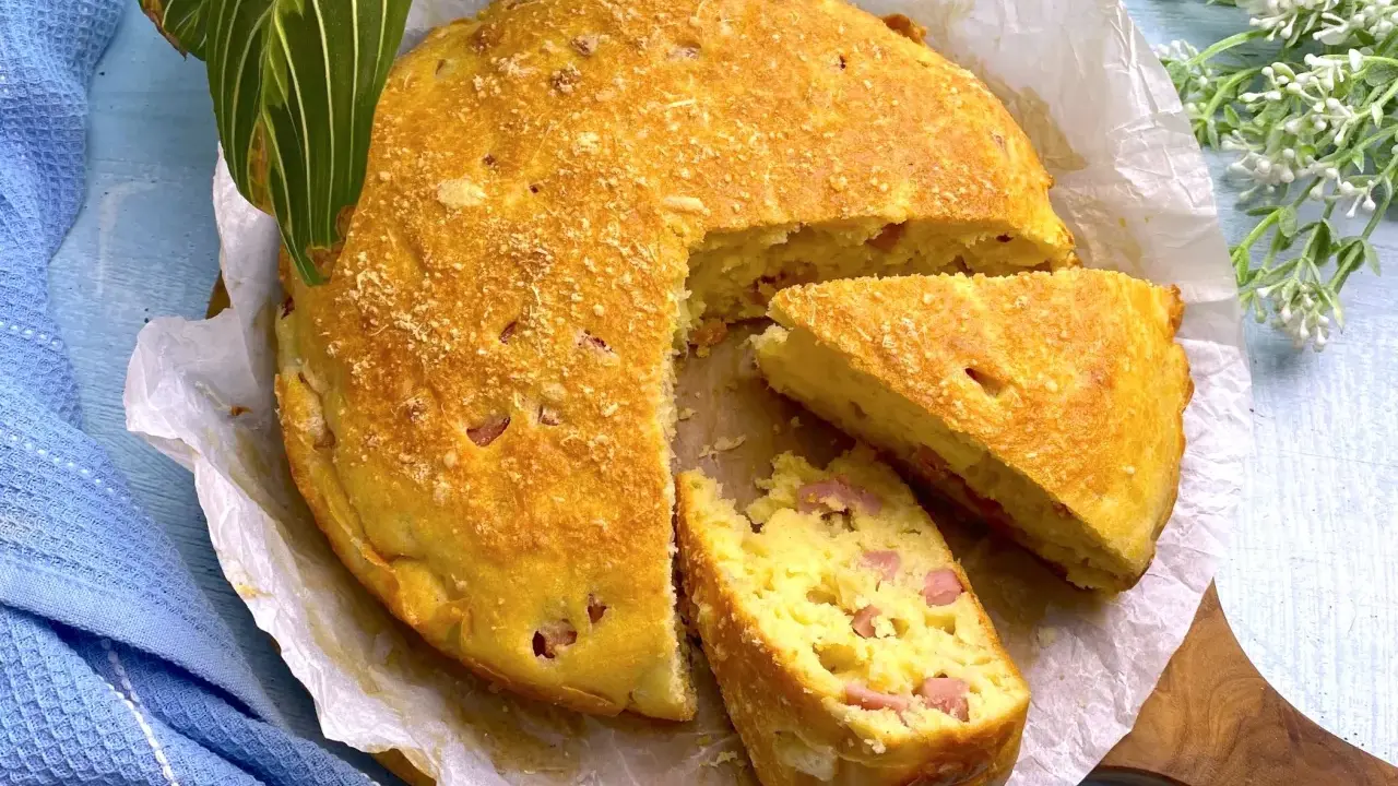 Una deliziosa torta salata prosciutto e formaggio, dorata e soffice, con una fetta tagliata per mostrare il ripieno.