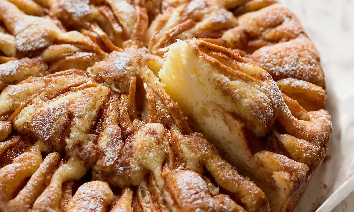 Una deliziosa torta di mele, cosparsa di zucchero a velo, con una fetta appena tolta che rivela la morbidezza dell'interno.