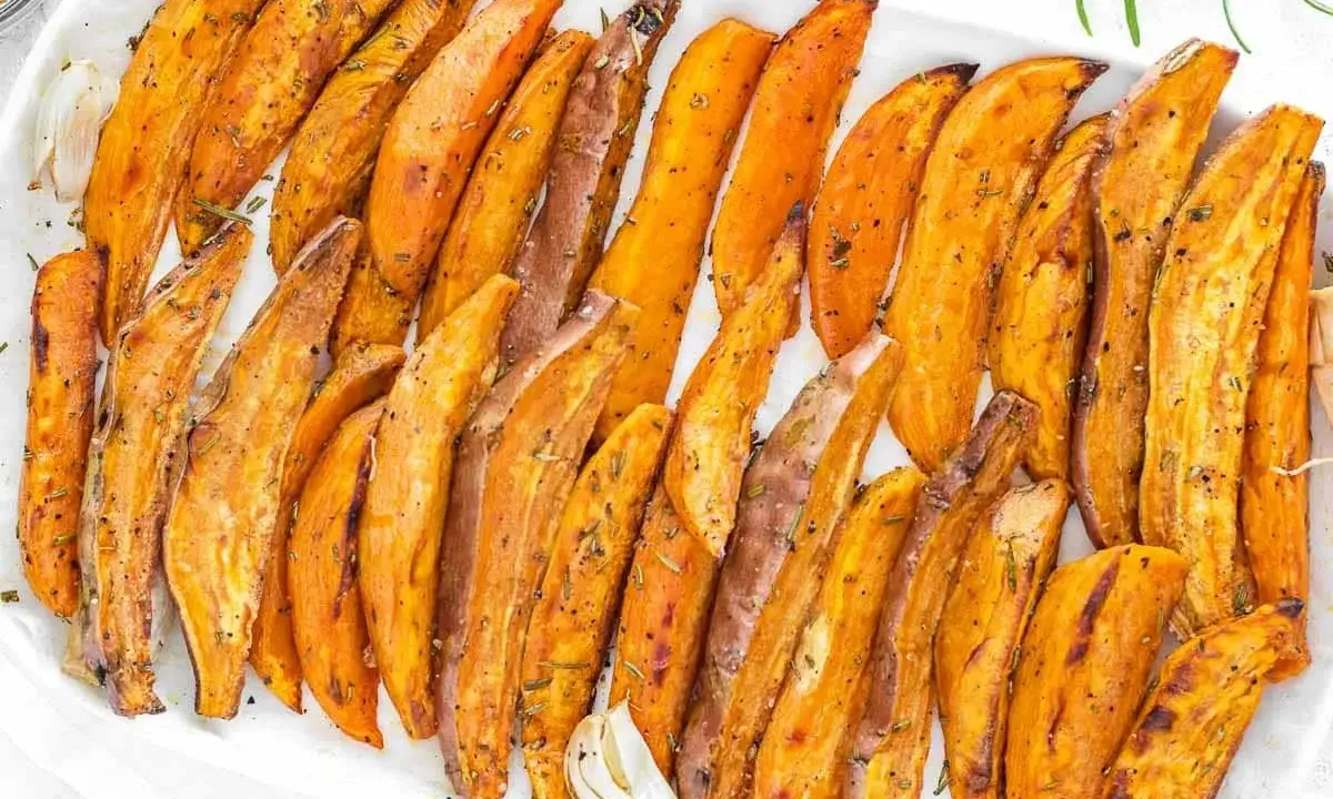 Patate dolci al forno, tagliate a spicchi e condite con erbe aromatiche, servite su un piatto bianco.
