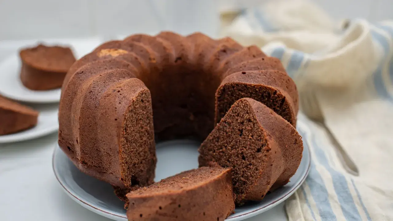 Un soffice ciambellone al cioccolato, appena sfornato, con alcune fette già pronte per essere gustate.