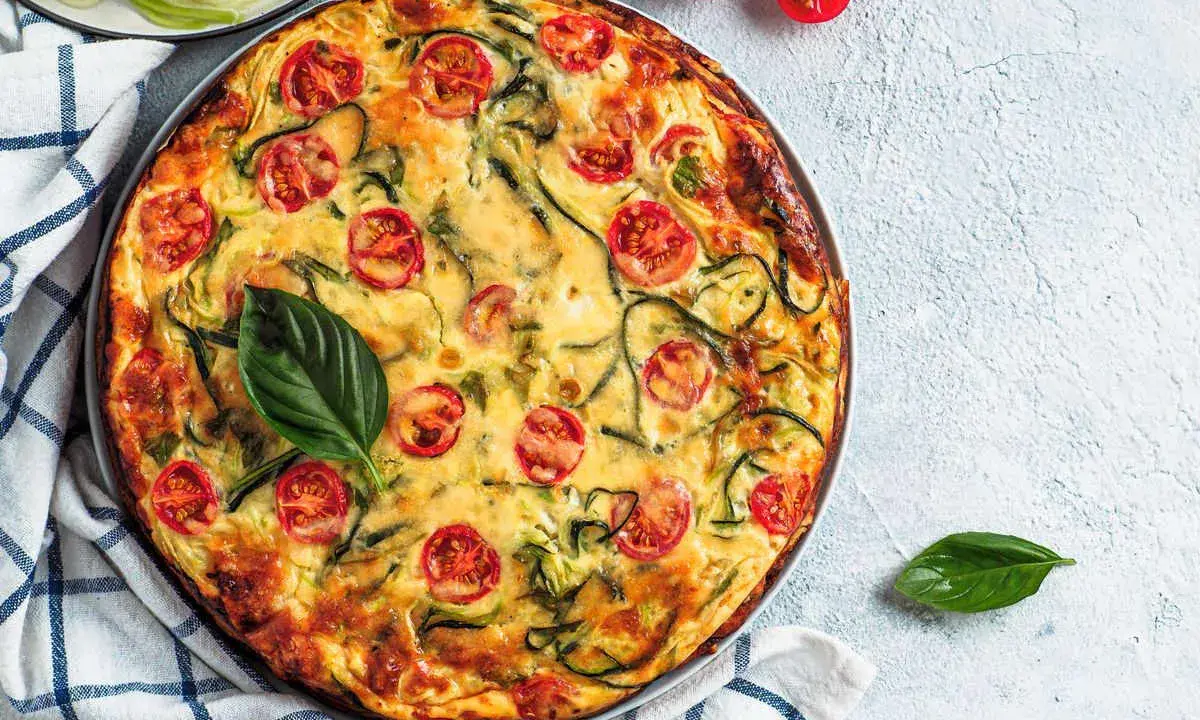 Torta salata vegana con zucchine e pomodorini, guarnita con basilico fresco.