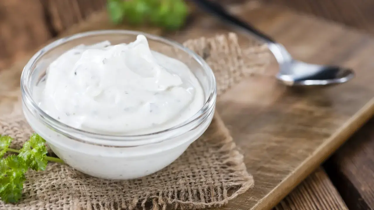 Una ciotola di panna acida cremosa, perfetta per la tua prossima ricetta. Un cucchiaino e un rametto di prezzemolo completano la scena rustica.