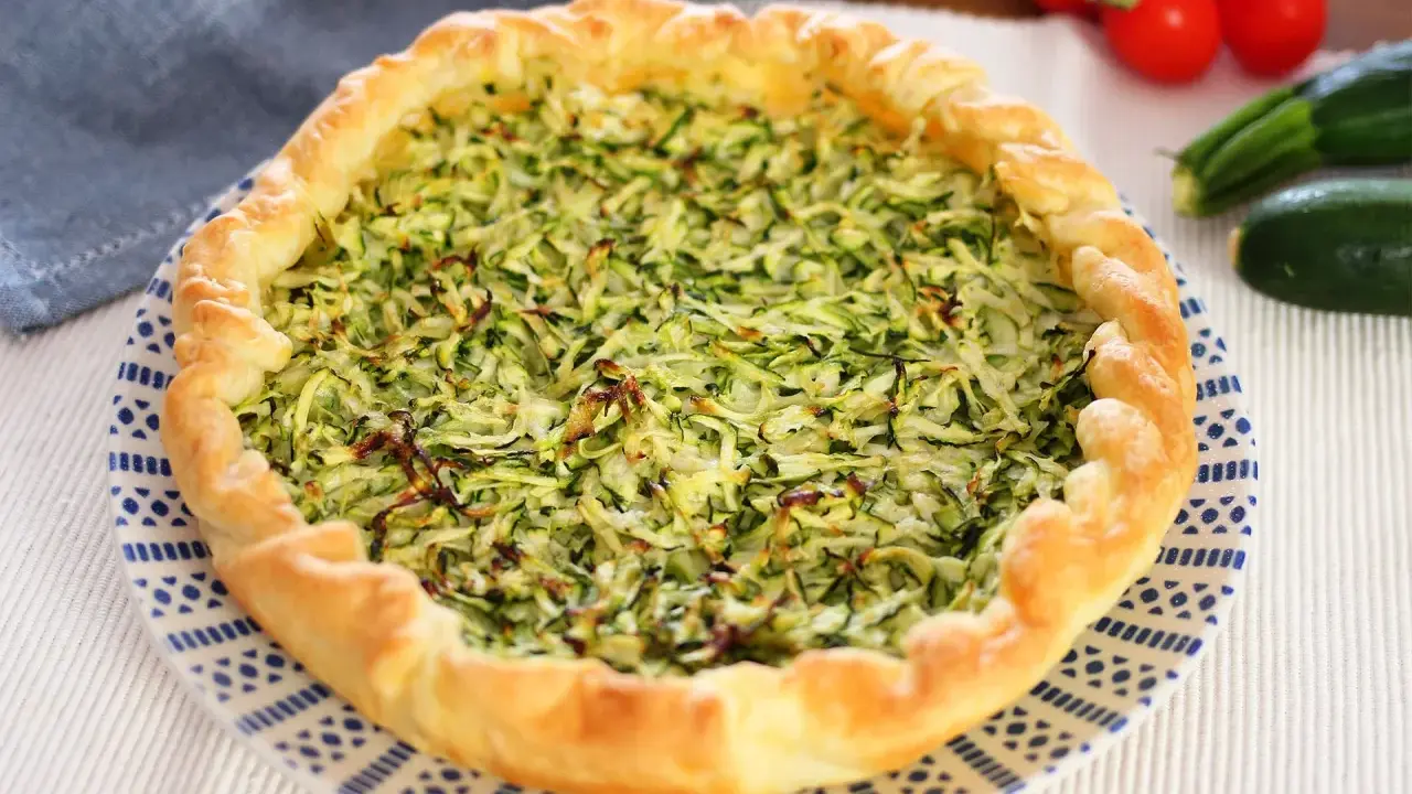 Torta salata con zucchine grattugiate e ricotta, con bordo dorato e decorazione blu su piatto bianco.