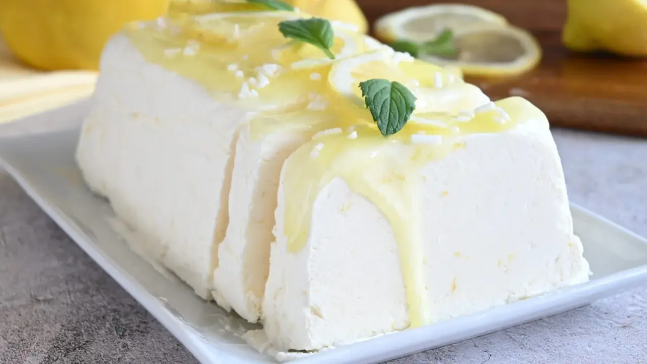 Un delizioso semifreddo al limone, guarnito con scorzette, menta e una glassa gialla, pronto per essere gustato.