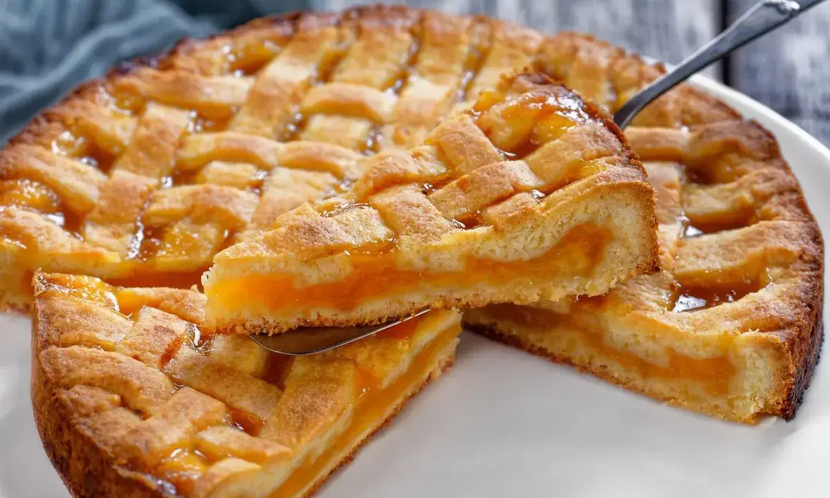 Una fetta di crostata senza glutine con ripieno di albicocche dorate, la sua pasta friabile e la griglia decorativa invitano a un assaggio goloso.