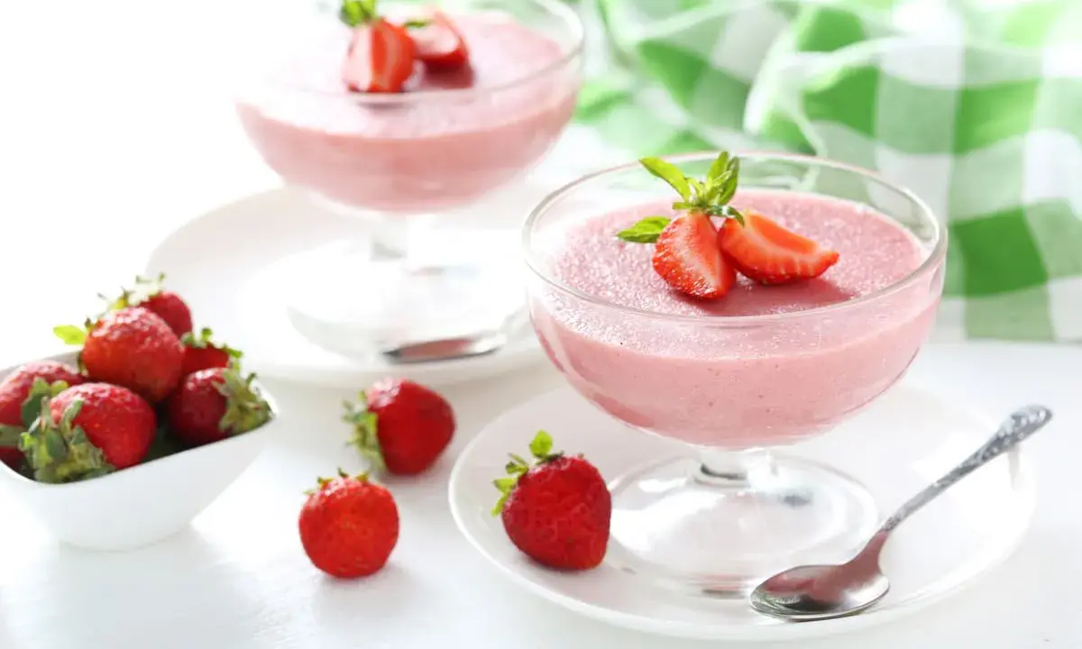 Deliziosa mousse di fragole in coppette di vetro, guarnita con fragole fresche e menta. Accanto, fragole in una ciotola bianca.
