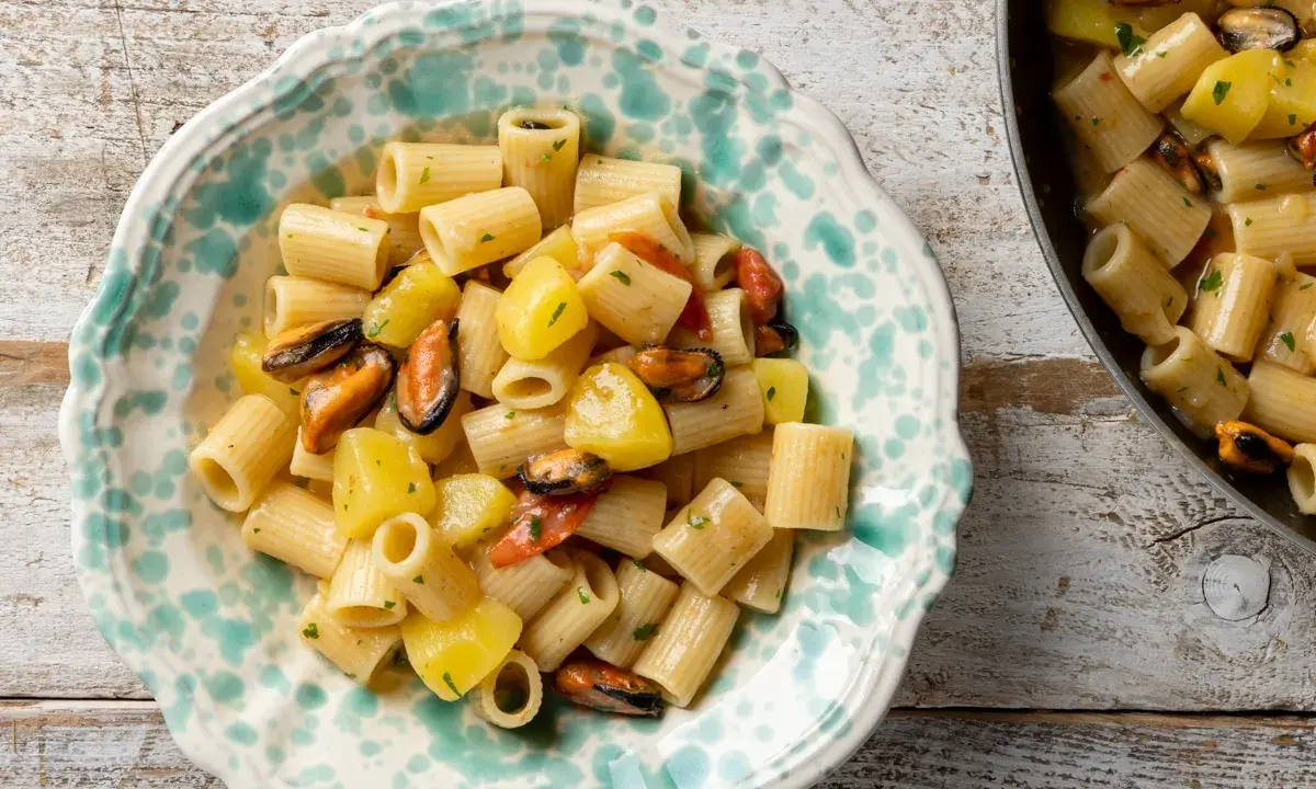 Un piatto di pasta patate e cozze, un classico della cucina italiana, servito in una ciotola decorata.