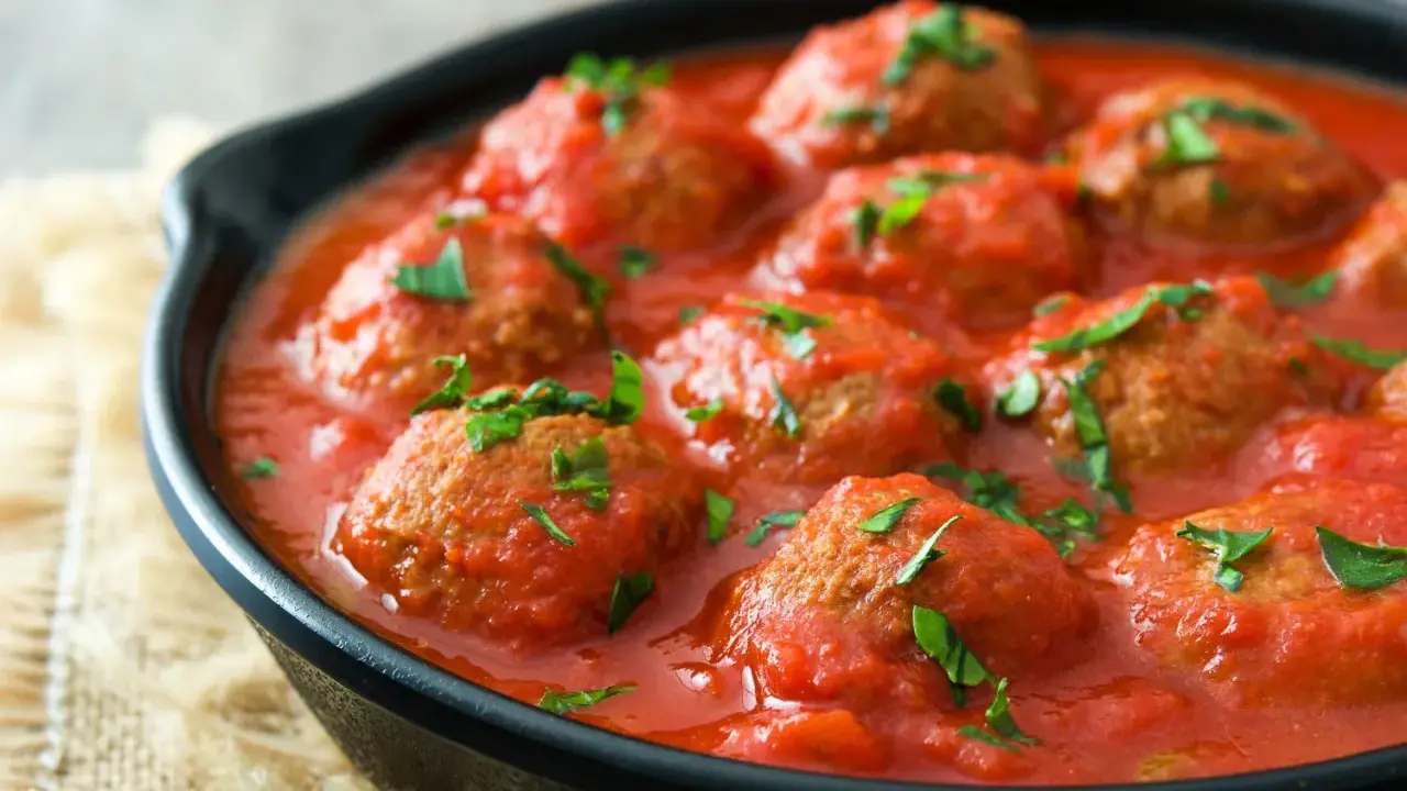 Polpette di carne succulente in salsa di pomodoro, guarnite con prezzemolo fresco, servite in una padella di ghisa.