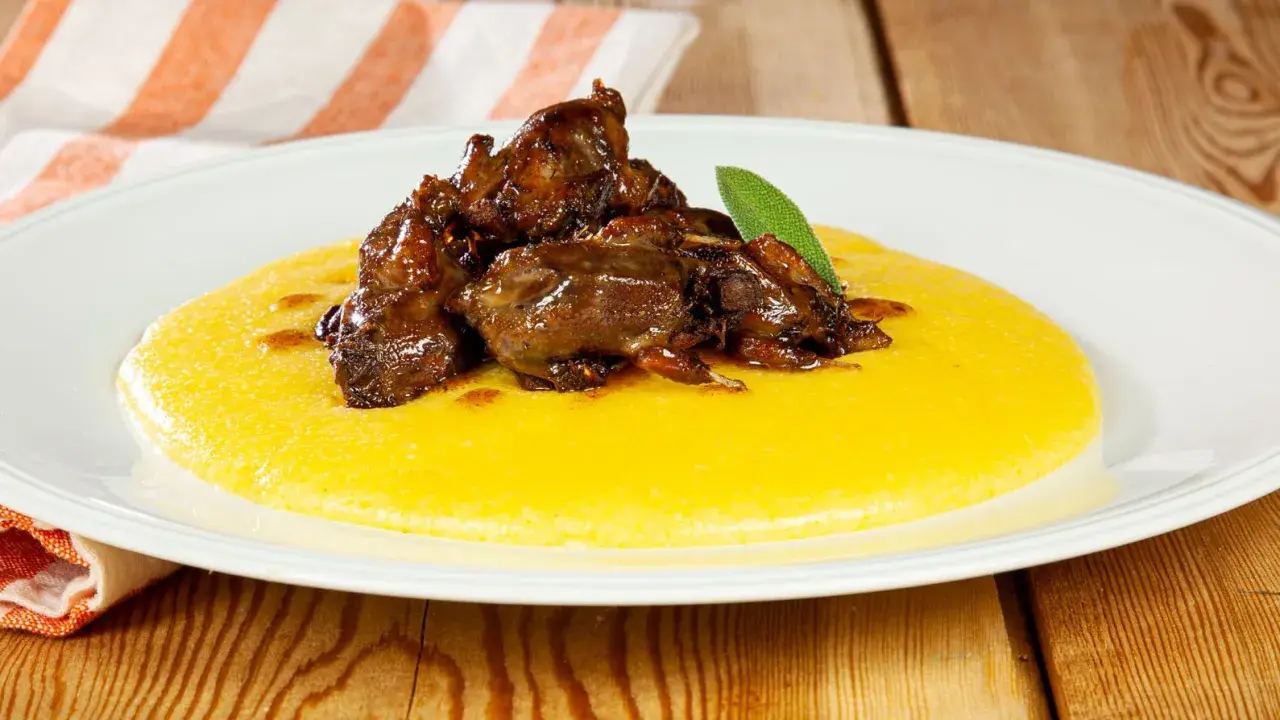 Piatto di polenta e osei, con uccellini scuri in umido e una foglia di salvia.