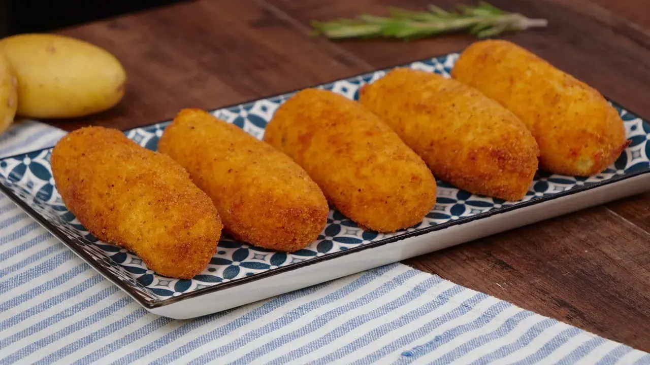 Cinque crocchette di patate dorate e croccanti su un piatto decorato, pronte per essere gustate.
