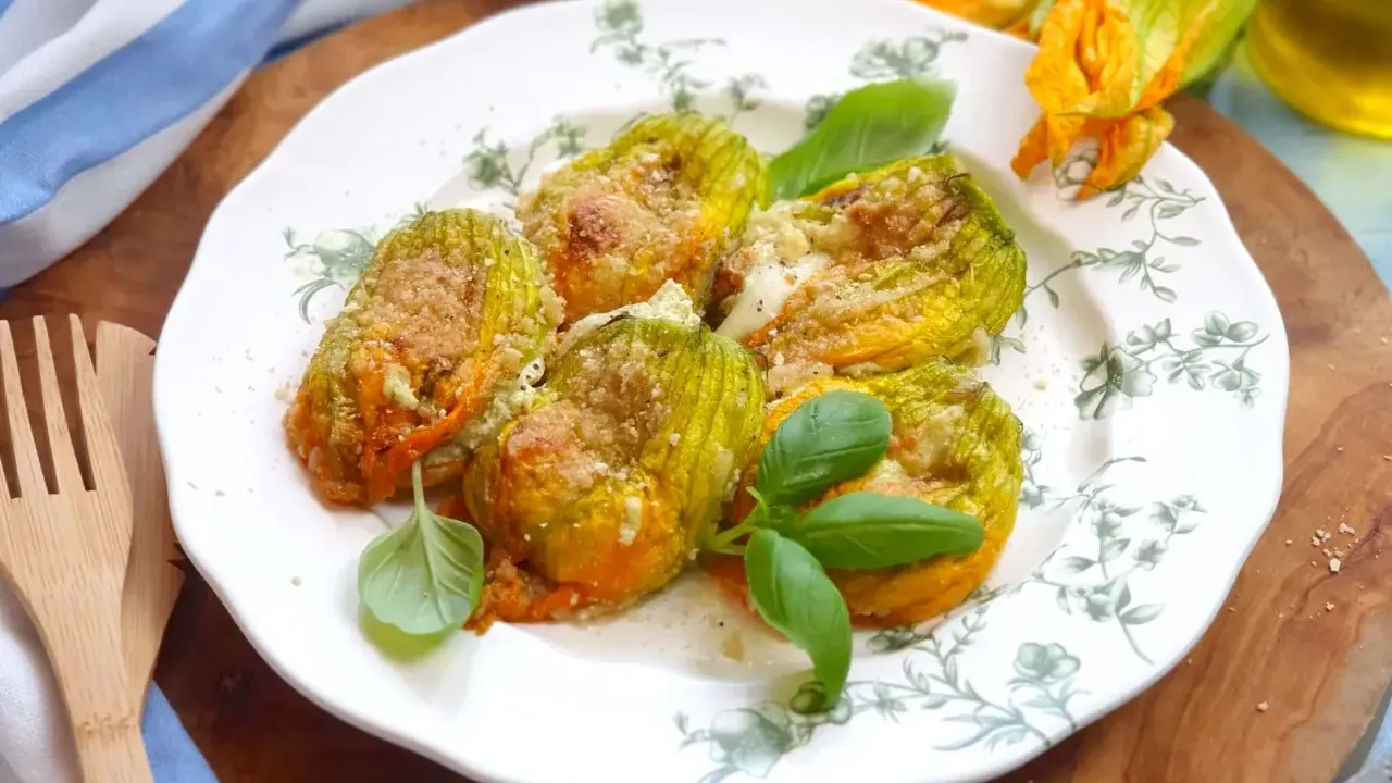 Deliziosi fiori di zucca al forno, ripieni e dorati, guarniti con basilico fresco su un piatto decorato.