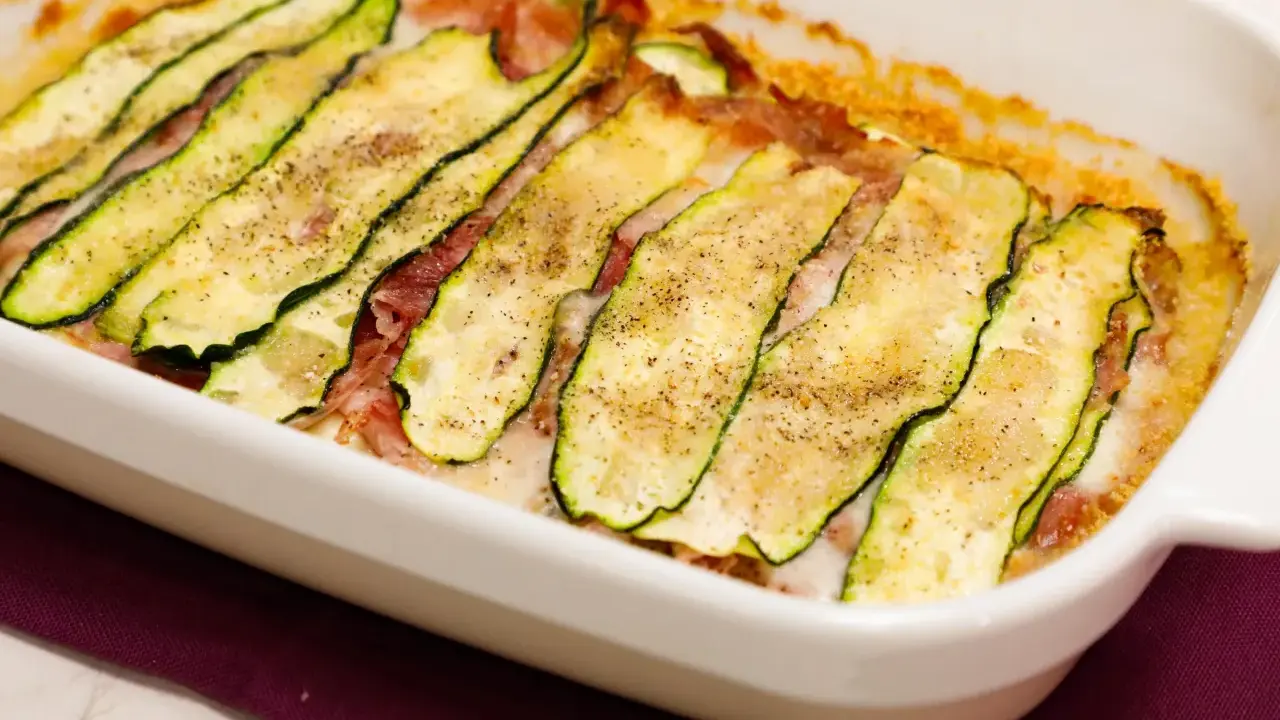 Sformato di zucchine appena sfornato, con fette sottili di zucchina grigliata, prosciutto e formaggio filante, condito con pepe nero.