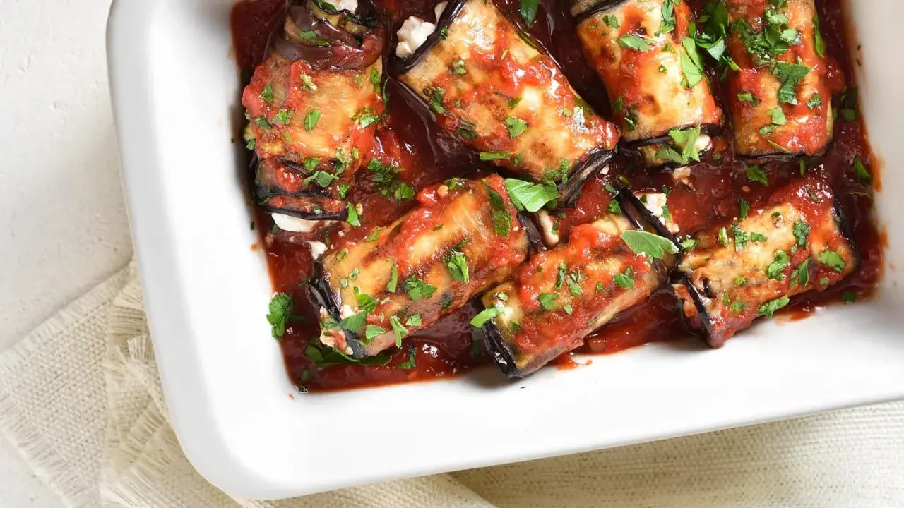 Involtini di melanzane ripieni di formaggio, cotti in sugo di pomodoro e guarniti con prezzemolo fresco.