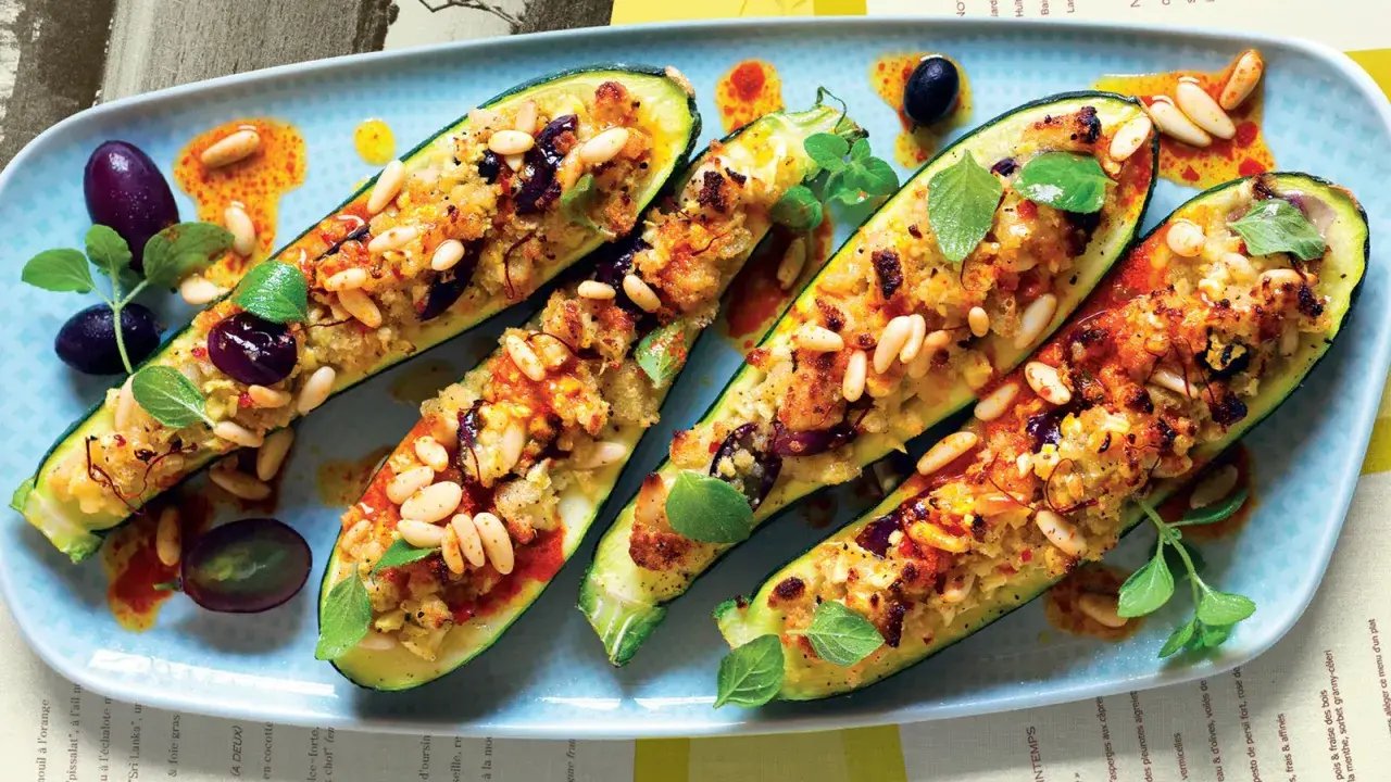 Zucchine ripiene vegetariane con pinoli, olive e erbe aromatiche, servite su un piatto azzurro con un filo d'olio piccante.