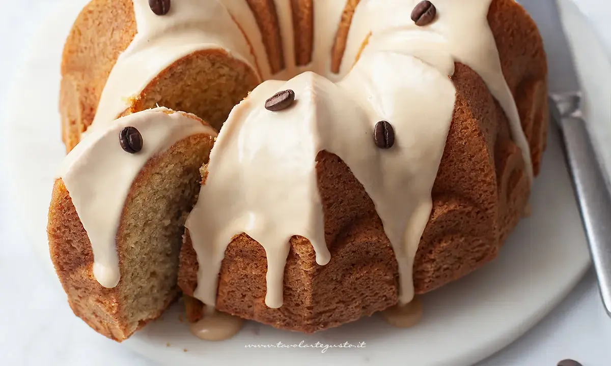 Deliziosa torta al caffè con glassa chiara e chicchi di caffè come decorazione. Una fetta è stata tagliata, mostrando la morbida consistenza interna.