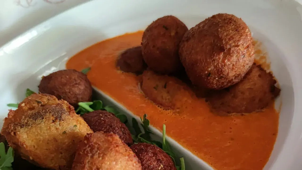 Polpette di pane dorate e croccanti, servite su una salsa rossa cremosa e guarnite con rucola fresca.