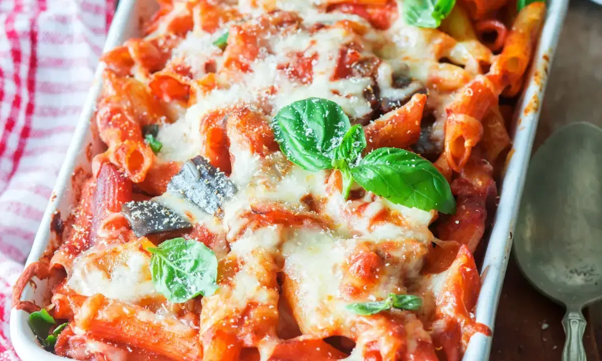Piatto fumante di pasta al forno con melanzane, ricoperta di formaggio fuso e basilico fresco.