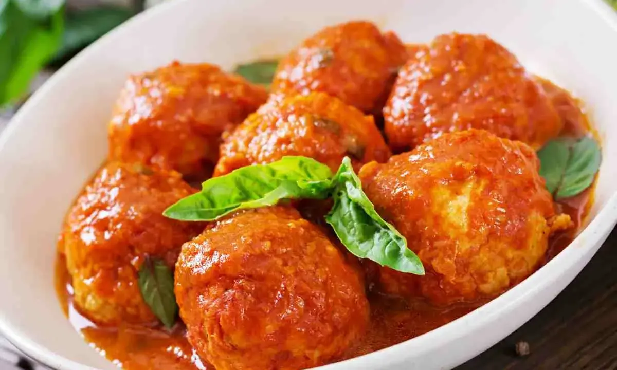 Polpette al sugo succulente in un piatto bianco, guarnite con foglie di basilico fresco. Un classico della cucina italiana.