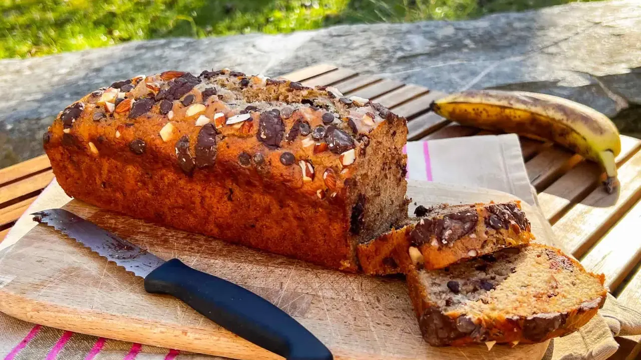 Delizioso banana bread vegano con gocce di cioccolato e mandorle, pronto per essere gustato all'aperto.