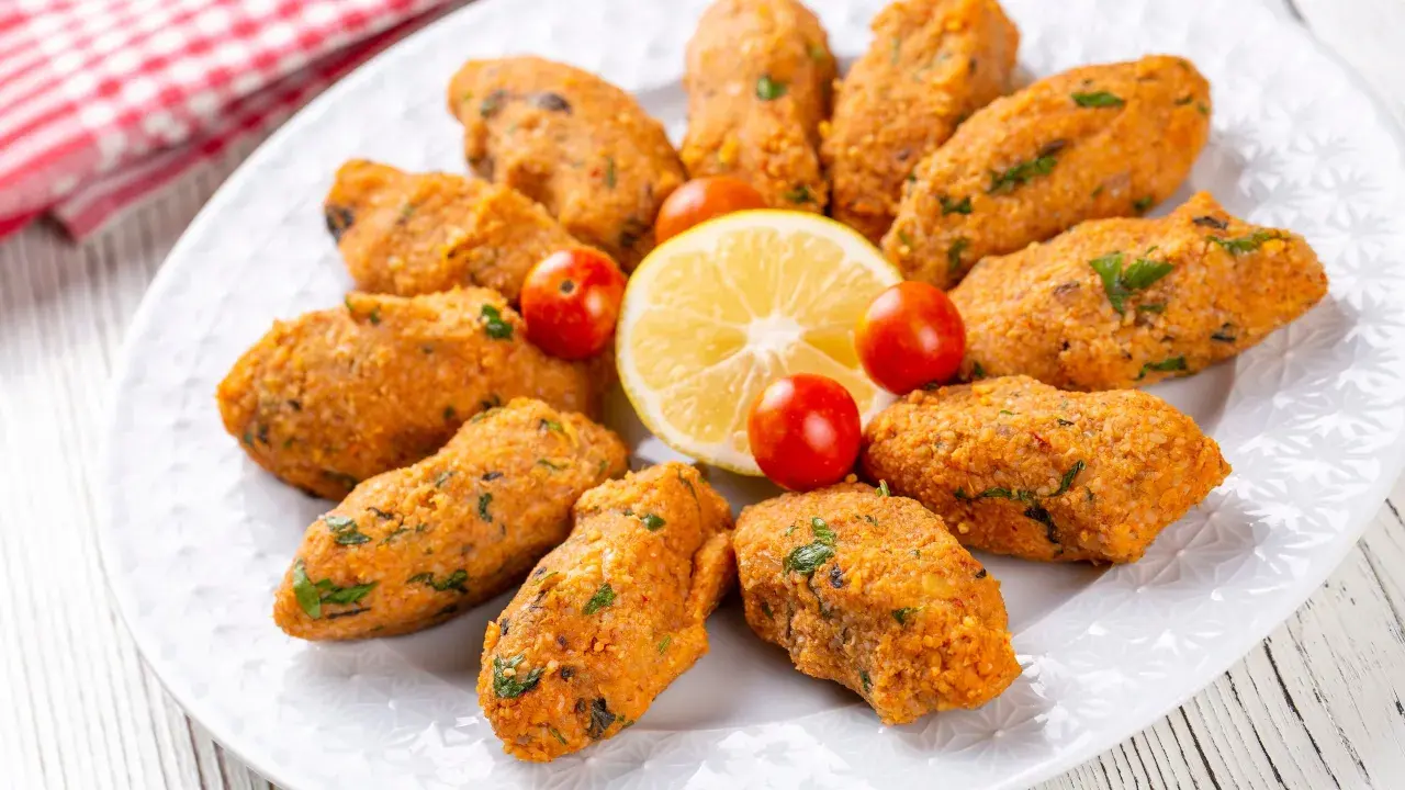 Deliziose polpette di lenticchie, disposte a cerchio su un piatto bianco, con spicchi di limone e pomodorini ciliegino.