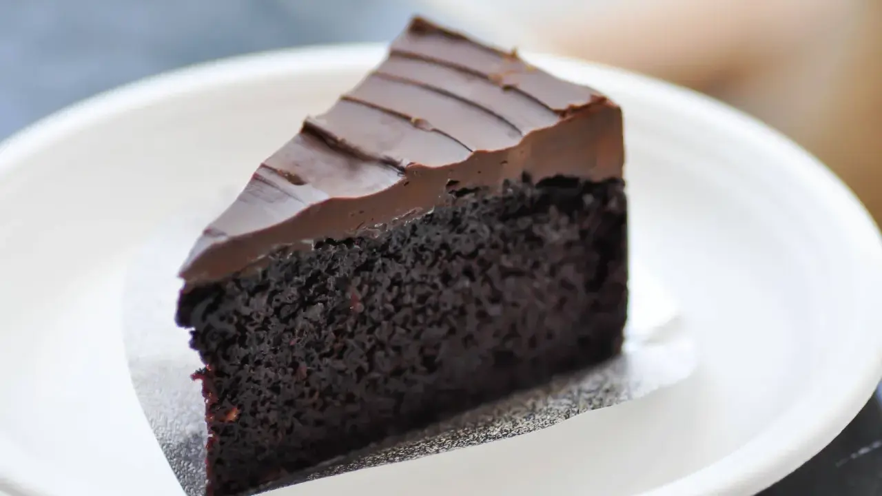 Una fetta di torta al cioccolato senza burro, soffice e ricoperta da glassa al cioccolato, servita su un piatto bianco.