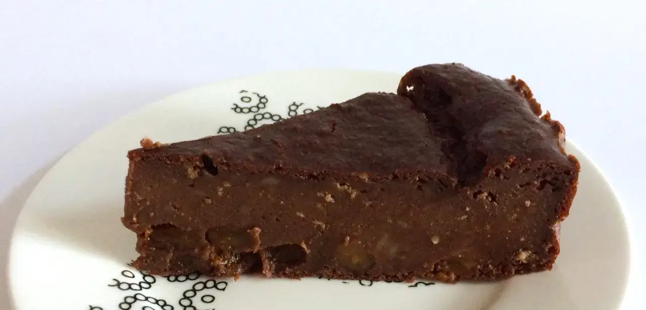 Una fetta di torta di pane al cioccolato, umida e ricca, con pezzi di frutta secca. La torta di pane ricetta della nonna, servita su un piatto bianco con decorazioni nere.