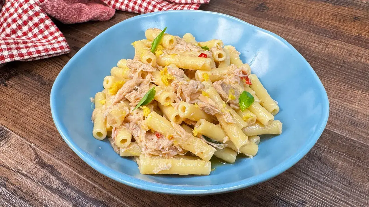 Piatto di pasta tonno e limone, condita con tonno sfilacciato, scorza di limone e basilico fresco, servita in un piatto blu.