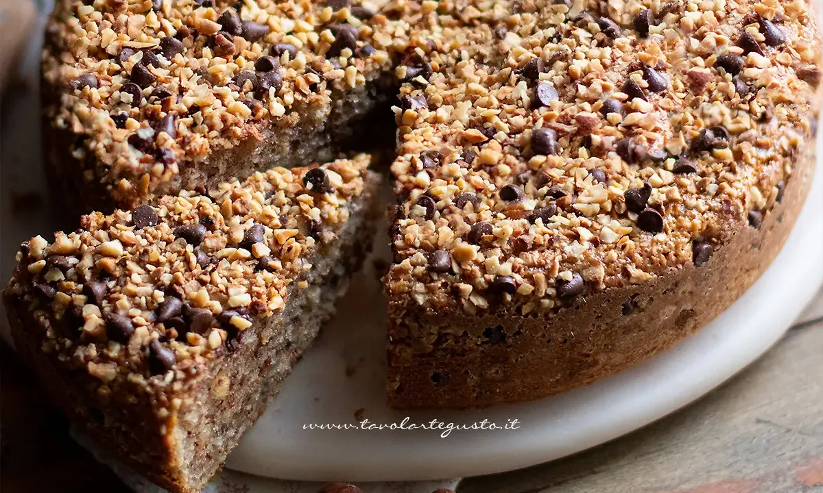 Una deliziosa torta di nocciole, ricoperta di granella di nocciole e gocce di cioccolato, con una fetta tagliata.