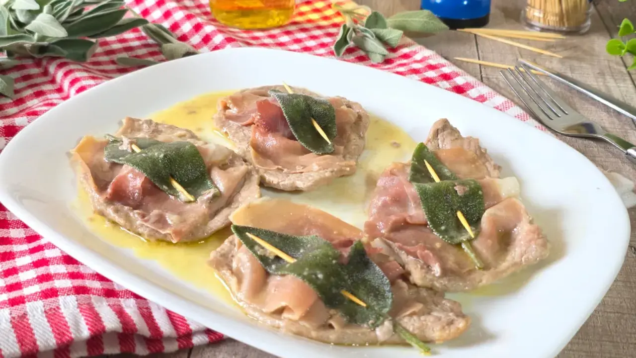 Saltimbocca alla romana: fettine di vitello con prosciutto e salvia, servite su un piatto bianco con salsa dorata.