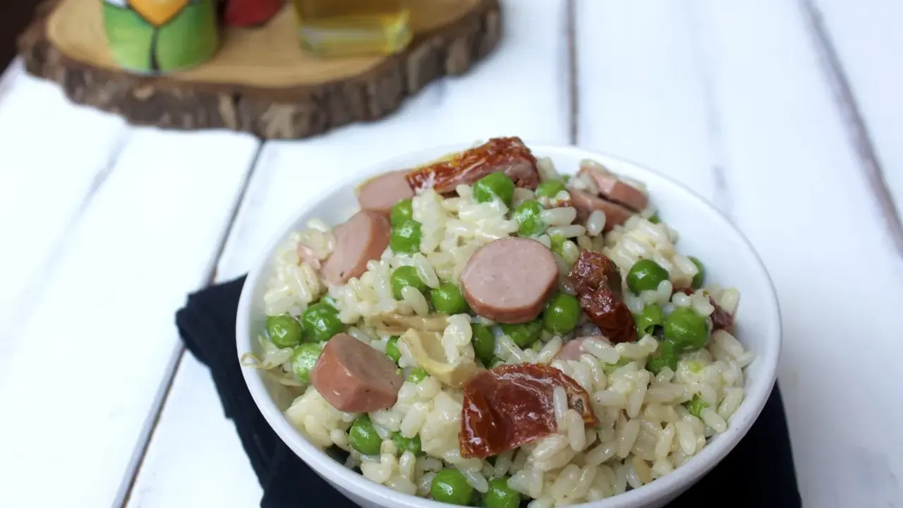 Una ciotola di insalata di riso con piselli, salsiccia e pomodori secchi, pronta per essere gustata.