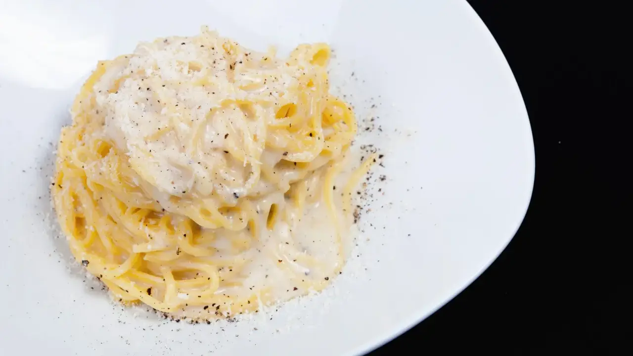 Un piatto di spaghetti cacio e pepe, cremosi e ricchi, cosparsi di pepe nero macinato fresco e formaggio grattugiato.