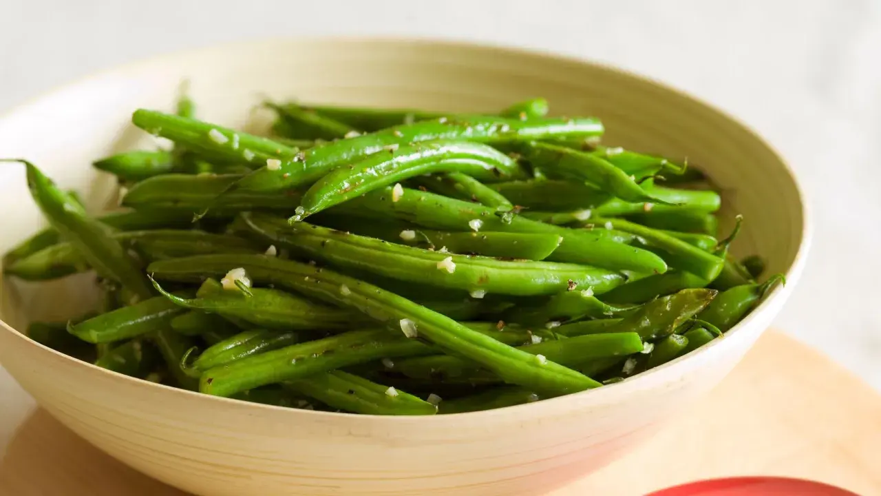 Fagiolini in padella conditi con aglio e pepe, serviti in una ciotola di legno.