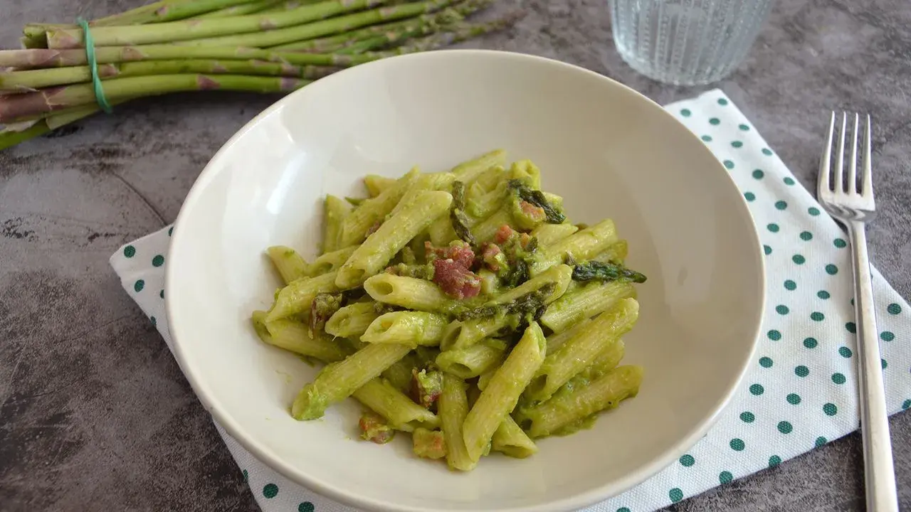 Penne cremose con asparagi freschi e cubetti di speck croccante, un piatto primaverile gustoso.