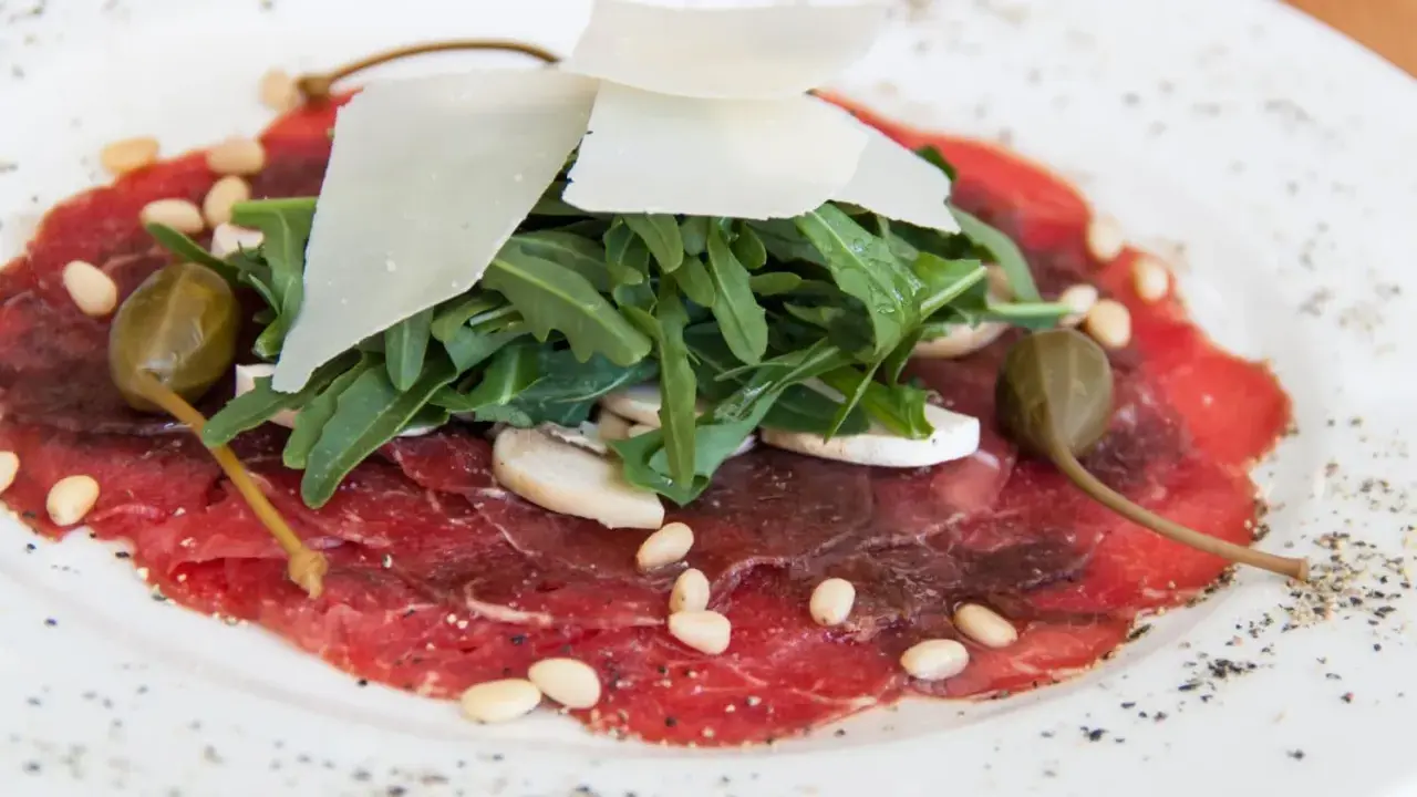 Delicato carpaccio di manzo con rucola, scaglie di parmigiano, pinoli, capperi e funghi champignon.