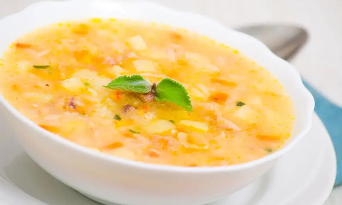Una ciotola di zuppa cremosa con pezzi di patate e riso, guarnita con una foglia verde. Un piatto confortante che sa di casa.
