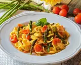 Piatto di orecchiette con asparagi freschi e pomodorini succosi, guarnito con basilico. Un classico della cucina italiana.