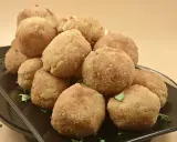 Un mucchio invitante di polpette di riso dorate e croccanti, guarnite con prezzemolo fresco, su un piatto scuro.