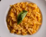 Un piatto di pasta patate e provola cremoso, con pezzi di patate e un rametto di basilico fresco.
