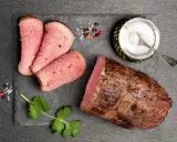 Una succulenta lombata di vitello, affettata e pronta per essere gustata, accompagnata da sale grosso, pepe e un rametto di coriandolo.