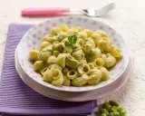 Piatto di pasta con le fave, condita con una crema verde e guarnita con menta. Un contorno di fave fresche completa la scena.