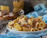 Piatto di pasta alla gricia fumante, guanciale croccante e pecorino romano grattugiato. Ingredienti freschi su un tavolo rustico.