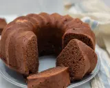 Un soffice ciambellone al cioccolato, appena sfornato, con alcune fette già pronte per essere gustate.