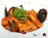Paccheri allo scoglio con cozze e pomodoro, guarniti con rucola fresca e petali di fiori.