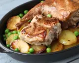 Un saporito coniglio in umido con patate arrosto e piselli verdi, servito in una cocotte scura.
