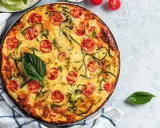 Torta salata vegana con zucchine e pomodorini, guarnita con basilico fresco.