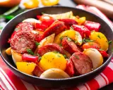 Salsiccia e patate in padella, un piatto saporito con peperoni rossi e gialli, cipolle e erbe aromatiche fresche.