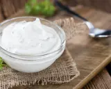 Una ciotola di panna acida cremosa, perfetta per la tua prossima ricetta. Un cucchiaino e un rametto di prezzemolo completano la scena rustica.